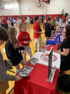 Tables set up in gymnasium with teenagers asking teachers questions